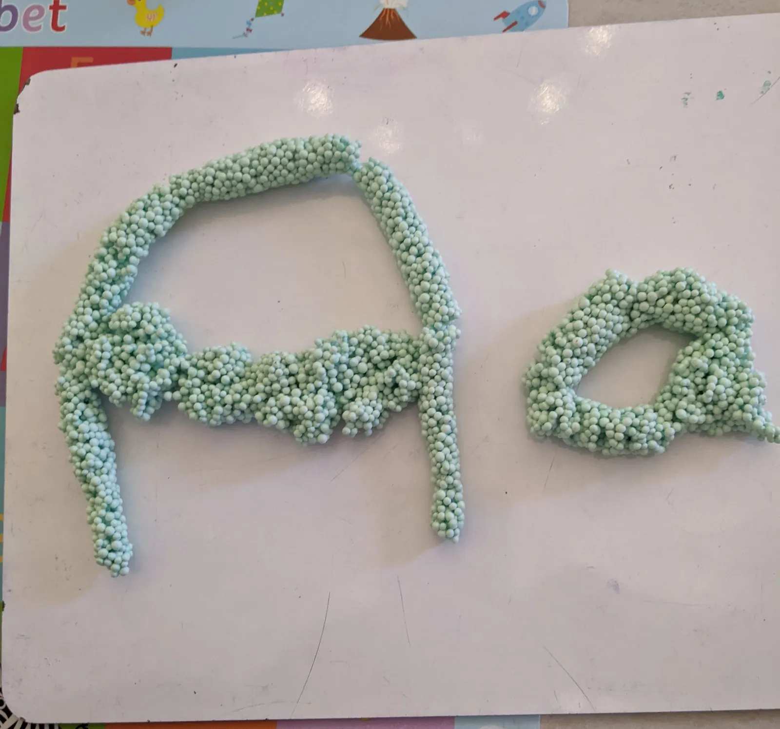 Capital and small letter a shaped from green foam beads on a whiteboard
