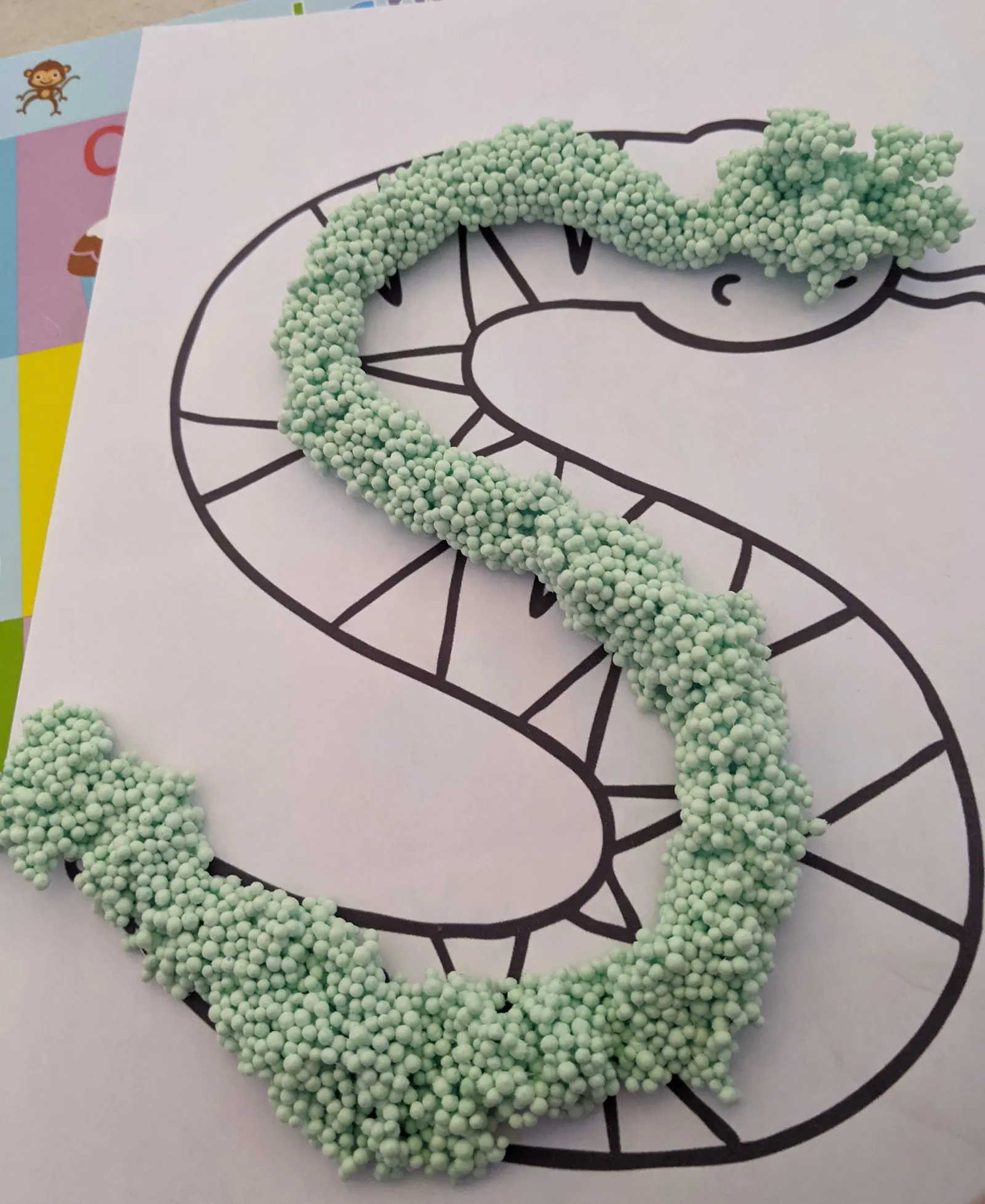 A letter s built from green foam beads over a printed snake, in a phonics lesson