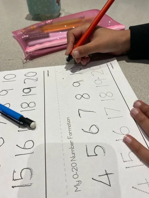 A child tracing numbers from 4 to 20 on a number formation sheet