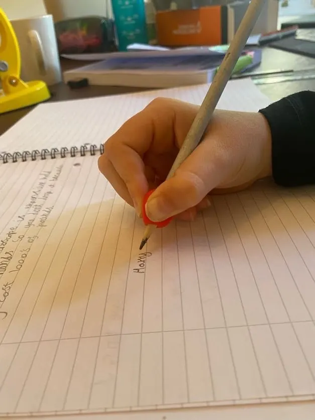 A child's hand holding a pencil fitted with a red pencil grip